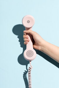 Woman's hand holding a pastel telephone on a blue background. Telecommunication.